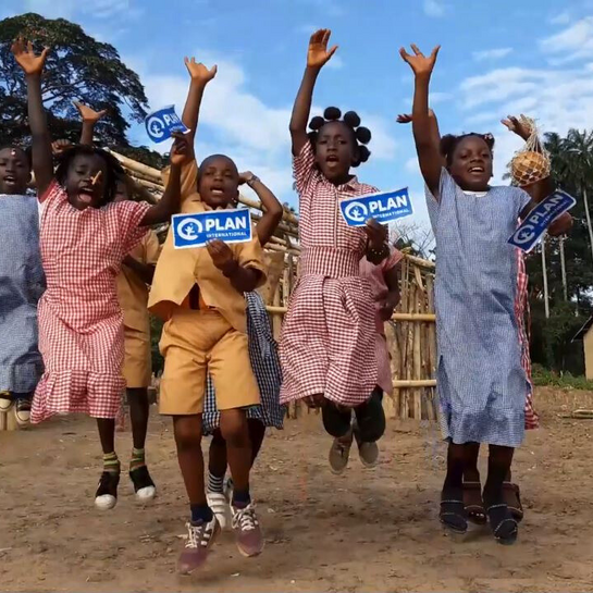 Eine Gruppe Kinder springt jauchzend in die Luft. Sie halten Plan International Schilder in der Hand.