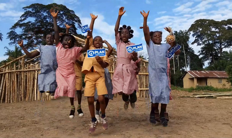 Eine Gruppe Kinder springt jauchzend in die Luft. Sie halten Plan International Schilder in der Hand.