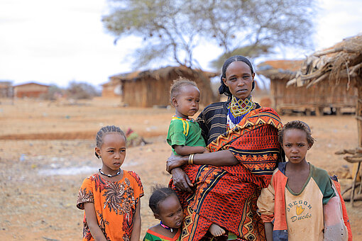 Eine Frau steht mit ihren vier Kindern in einer trockenen Landschaft, ein Kind hält sie im Arm.