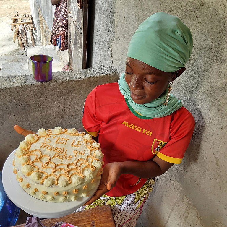 Eine junge Frau hält eine fertige Torte in der Hand, die mit Sahne verziert ist