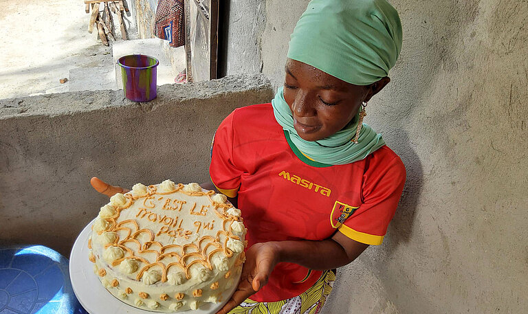 Eine junge Frau hält eine fertige Torte in der Hand, die mit Sahne verziert ist