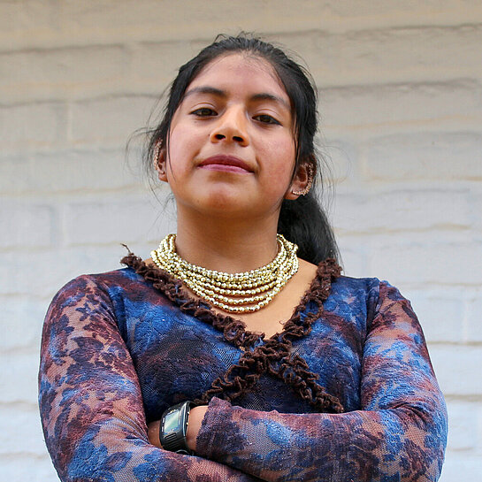 Yadira steht selbstbewusst mit verschränkten Armen vor einer Wand.