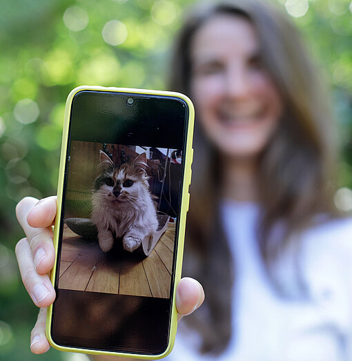 Eine Frau hält ein Handy in die Kamera, auf dem Display ist das Foto einer Katze zu sehen