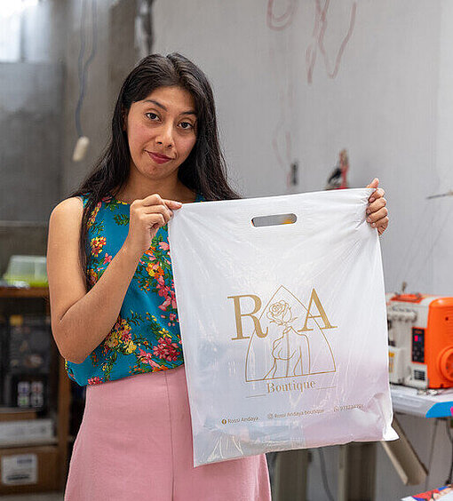 Eine junge Frau hält eine Tasche mit dem Logo einer Boutique in die Höhe.