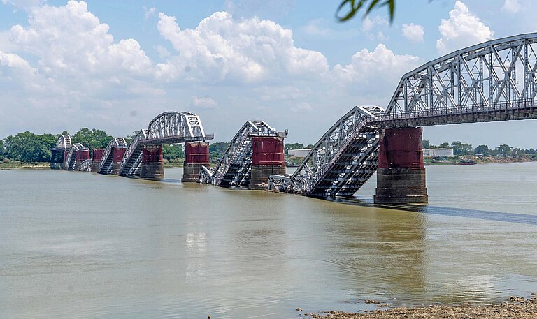 Blick auf eine Eisenbrücke, deren Bögen zerstört halb abgestürzt im Wasser eines Flusses liegen
