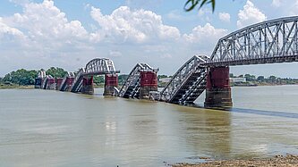 Blick auf eine Eisenbrücke, deren Bögen zerstört halb abgestürzt im Wasser eines Flusses liegen