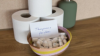 Drei Rollen Toilettenpapier und eine Schüssel mit Tampons