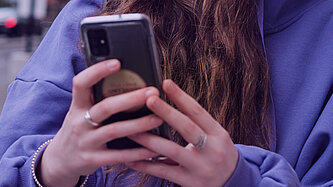 Eine junge Person hält ihr Smartphone in der Hand und ist am Tippen.
