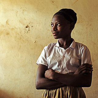 Eine junge Frau steht in einem Raum, sie hat die Arme verschränkt und schaut zur Seite