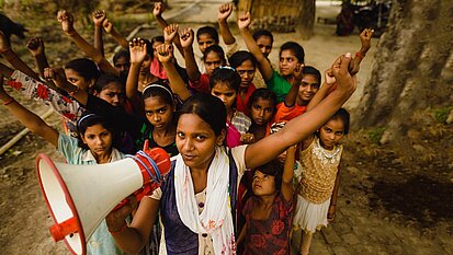 Eine Gruppe indischer Mädchen mit erhobenen Fäusten. Das Mädchen im Vordergrund hält ein Megafon.