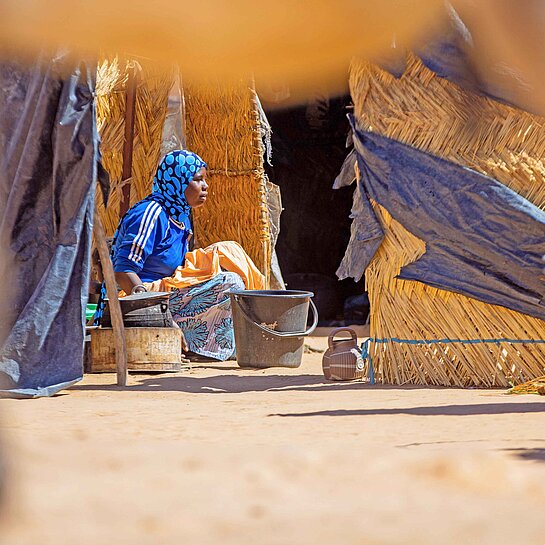 Eine Frau sitzt vor einer Strohhütte in Niger