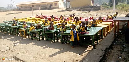 Kinder sitzen an Schultischen auf einem Hof