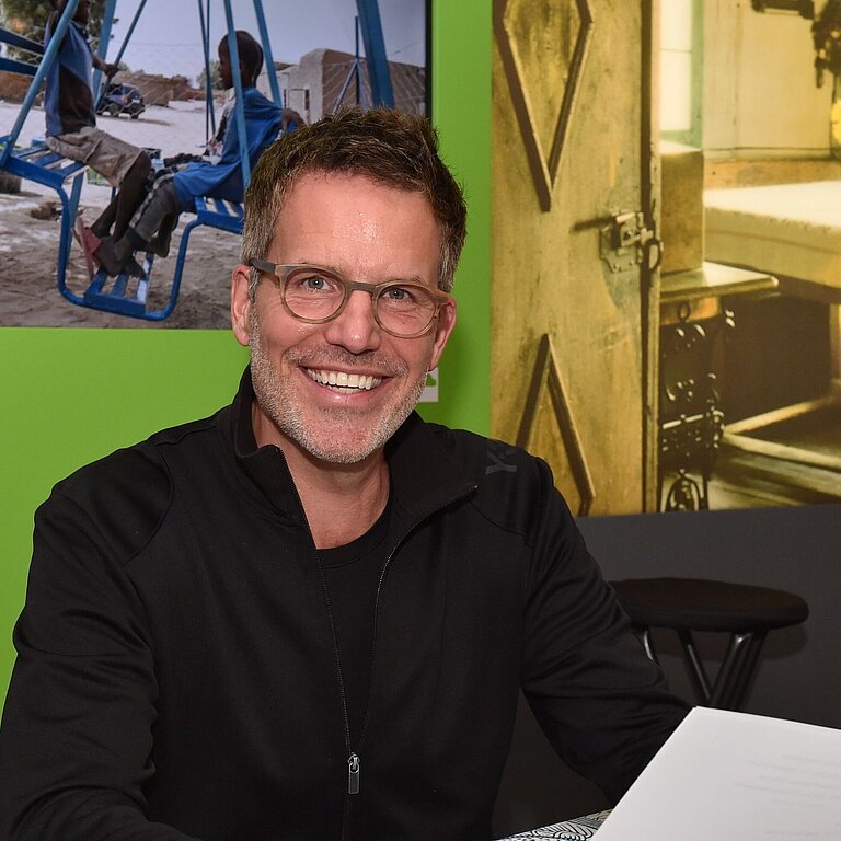 Schauspieler Tim Bergmann sitzt an einem Tisch und hält ein Blatt Papier in der Hand