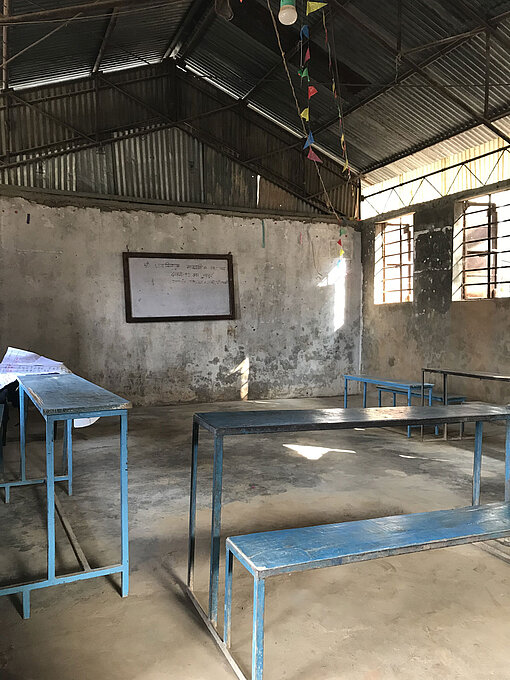 Die Jugendlichen haben eine Schule besucht, um den nepalesischen Kontext besser kennenzulernen. Das Bild zeigt ein leeres Klassenzimmer in Nepal. Man sieht drei Schulbänke und eine Tafel.