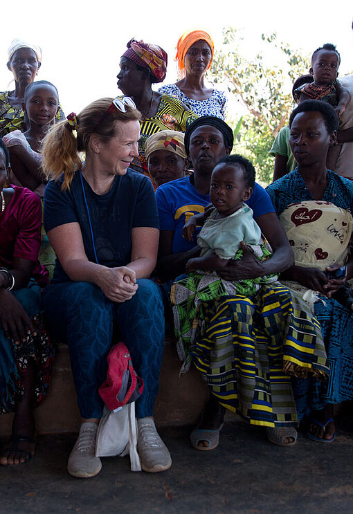 Marion Kracht sitzt inmitten von ruandischen Kindern und Erwachsenen auf einer Bank