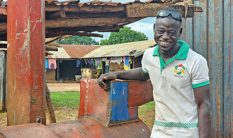 Ein schwarzer junger Mann lehnt lächelnd und lässig an einem Metallamboss