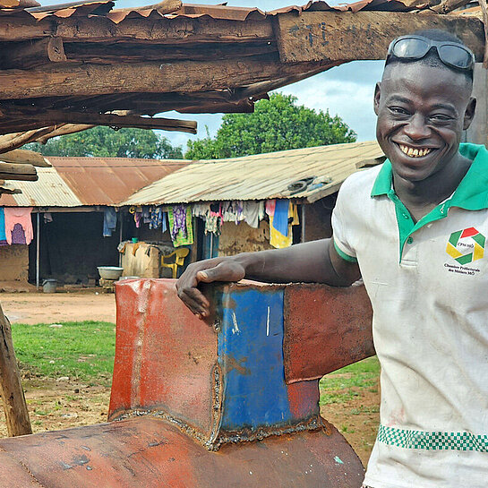 Ein schwarzer junger Mann lehnt lächelnd und lässig an einem Metallamboss