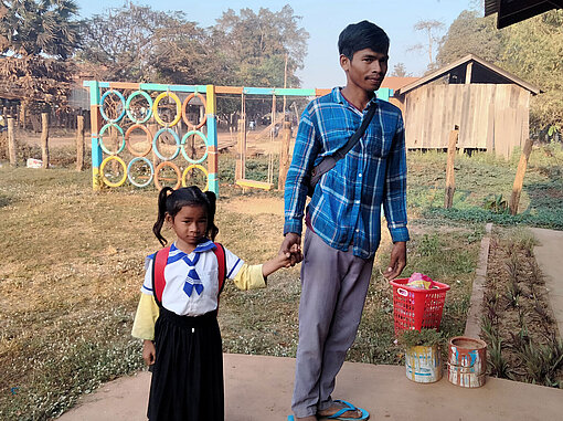 Plan International bestärkt Väter darin, eine größere Rolle im Leben ihrer Kinder einzunehmen. Ein Vater hält seine Tochter an der Hand. Sie trägt eine Vorschuluniform.