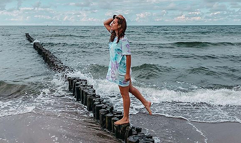 Luisa steht auf Holzpfahl im Meer.