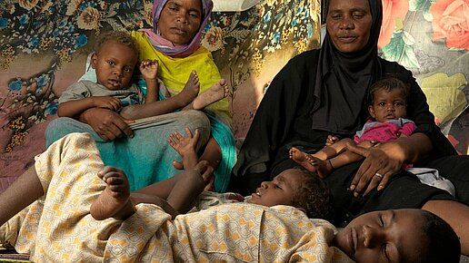 Eine Frau mit ihren Kindern, von denen zwei (liegend) mit Behinderung leben.