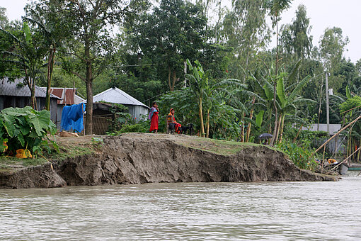 Hochwasser in Bangladesch Ein abgebrochenes Ufer, direkt dahinter steht ein Haus, davor sieht man Hochwasser