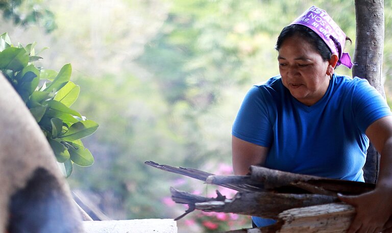 Bäckerin in Honduras legt Feuerholz für Lehmofen nach