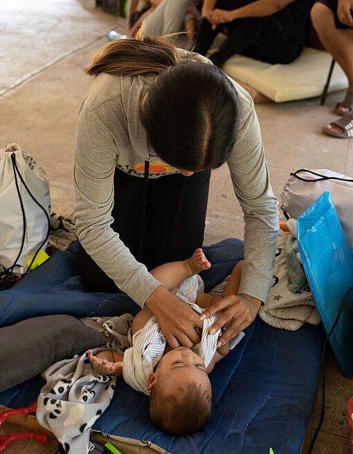 Eine Frau kniet auf einer Matte auf dem Boden und wickelt ein Baby