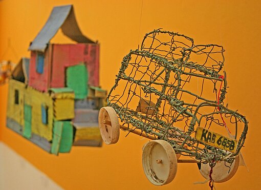 Hier haben Kinder aus Pappe ein Haus und aus Draht ein Auto gebaut Ein Papphaus und ein Drahtauto hängen von der Decke als Teil einer Ausstellung über Kinderspielzeug