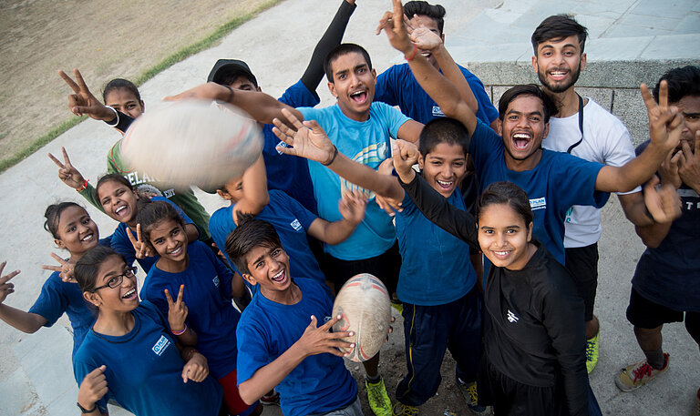 Gruppe von Jugendlichen wirft Rugby in die Luft.
