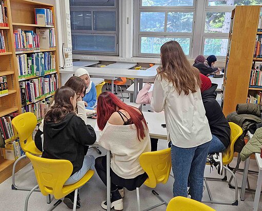 Hier entstehen gemeinsam mit Plan-Botschafterin Carina Roth neue Idee für die Start-ups von morgen In einer Bibliothek arbeiten Kinder mit einer Frau an einem Text