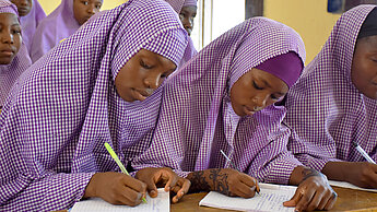 Mädchen sitzen in einem Klassenzimmer und schreiben in ihre Hefte