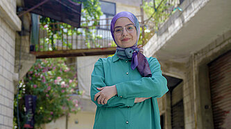 Junge Frau mit Kopftuch und verschränkten Armen in einer leeren Straße