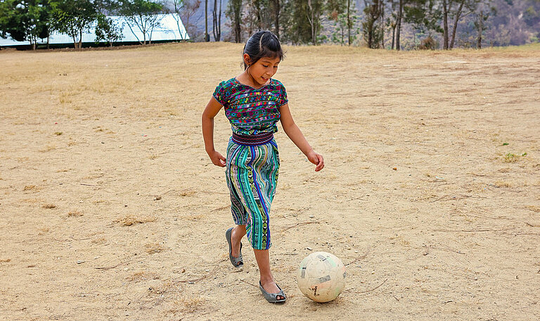 Ein Mädchen kickt einen Fußball über einen staubigen Platz