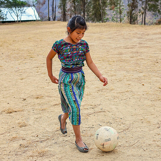 Ein Mädchen kickt einen Fußball über einen staubigen Platz