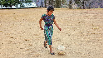 Ein Mädchen kickt einen Fußball über einen staubigen Platz