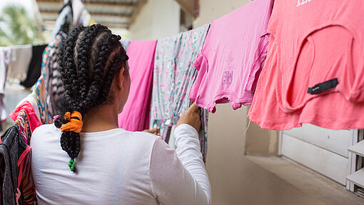 In fast allen sozialen Aspekten trifft die Krankheit Frauen härter. Mädchen hängt pinke T-Shirts an Wäscheleine auf.
