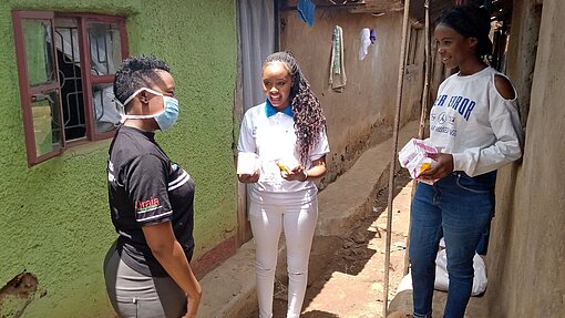 Plan-Aktivistin Nisera (links) versorgt junge Frauen in Kibera mit Hygieneartikeln. Drei junge Frauen unterhalten sich.
