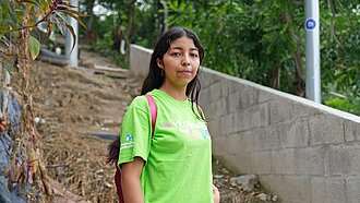 Eine junge Frau mit grünem T-Shirt steht an einem Trampelpfad im Unterholz