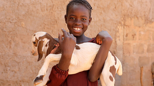 Ainee hält eine Baby-Ziege auf dem Arm.