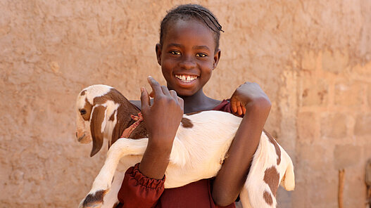 Ainee hält eine Baby-Ziege auf dem Arm.