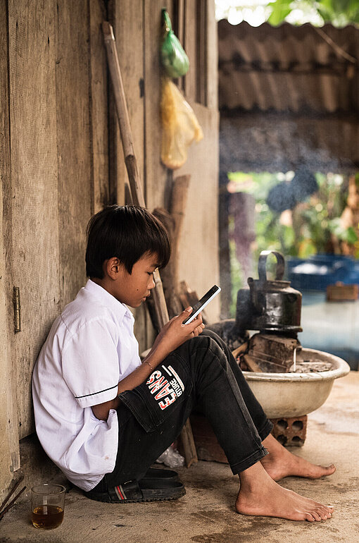 Der Schutz vor Cyber-Mobbing und Missbrauch soll auch in der vietnamesischen Provinz greifen Ein Junge hockt auf einer Bastmatte und liest auf seinem Smartphone.