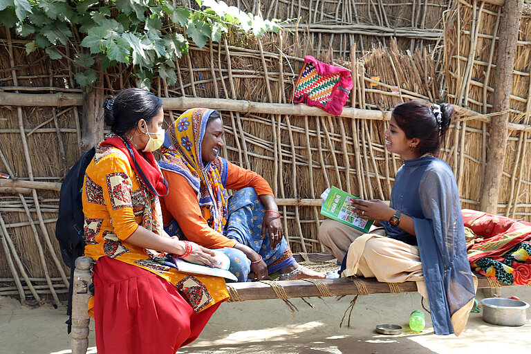 Eine junge Frau sitzt mit zwei älteren Frau auf dem Boden und spricht mit ihnen über Kinderheirat