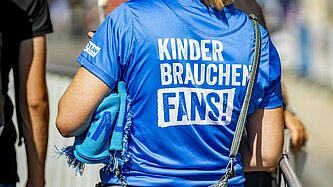 Eine Frau trägt ein T-Shirt der Kampagne "Kinder brauchen Fans!"