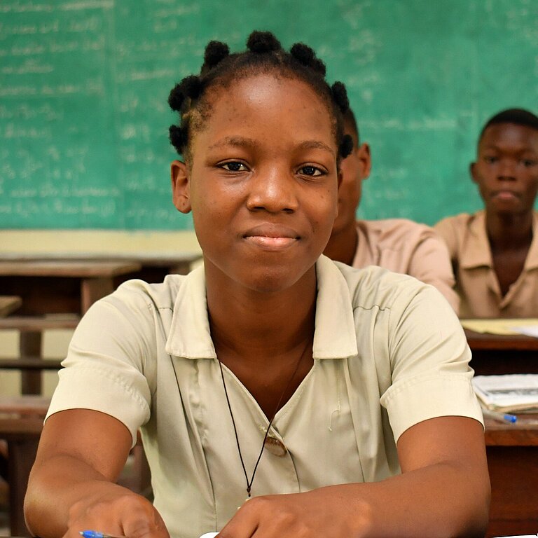 Monique sitzt an ihrem Platz im Klassenzimmer und folgt dem Unterricht