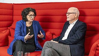 Eine Frau und ein Mann sitzen im Gespräch auf einem Sofa