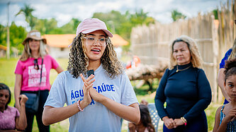 Eine junge Frau in mit rosa Cap steht in einem Kreis Menschen und spricht mit ihnen.