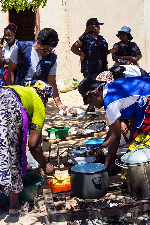 Frauen geben Essen aus, das in großen Töpfen auf dem Boden steht