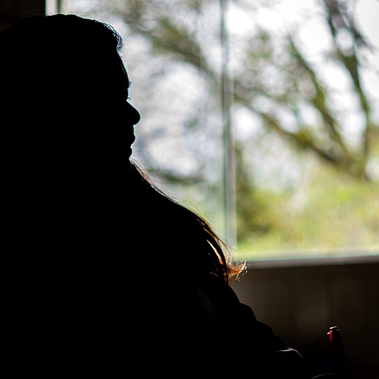 Eine Silhouette einer Frau vor einem Fenster sitzend.