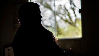 Eine Silhouette einer Frau vor einem Fenster sitzend.