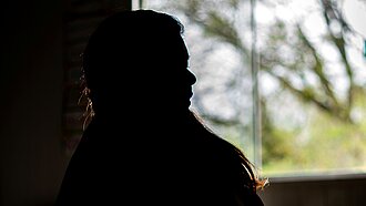 Eine Silhouette einer Frau vor einem Fenster sitzend.